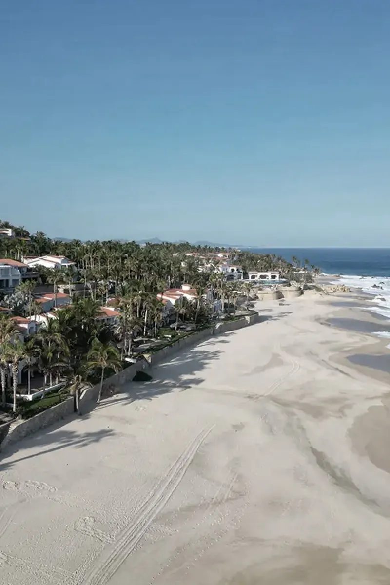An aerial of the Villas Del Mar beachfront, terracotta-roofed homes behind palms along the sand.