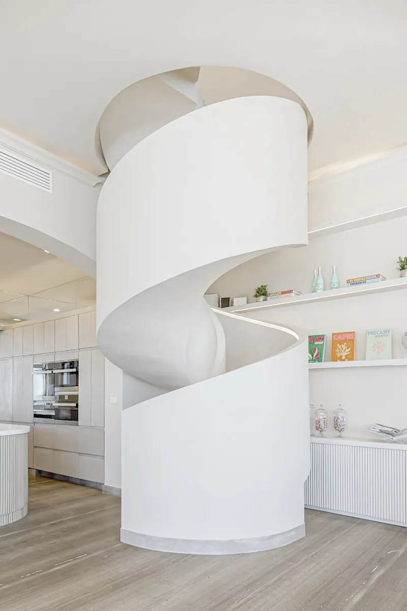 The sculptural white spiral staircase rising between the kitchen and the shelving.