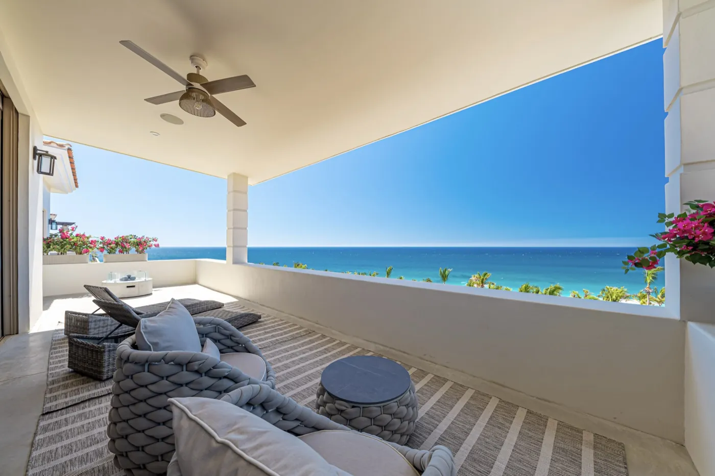 Shaded balcony with woven loungers and bougainvillea overlooking the turquoise sea and coastline.