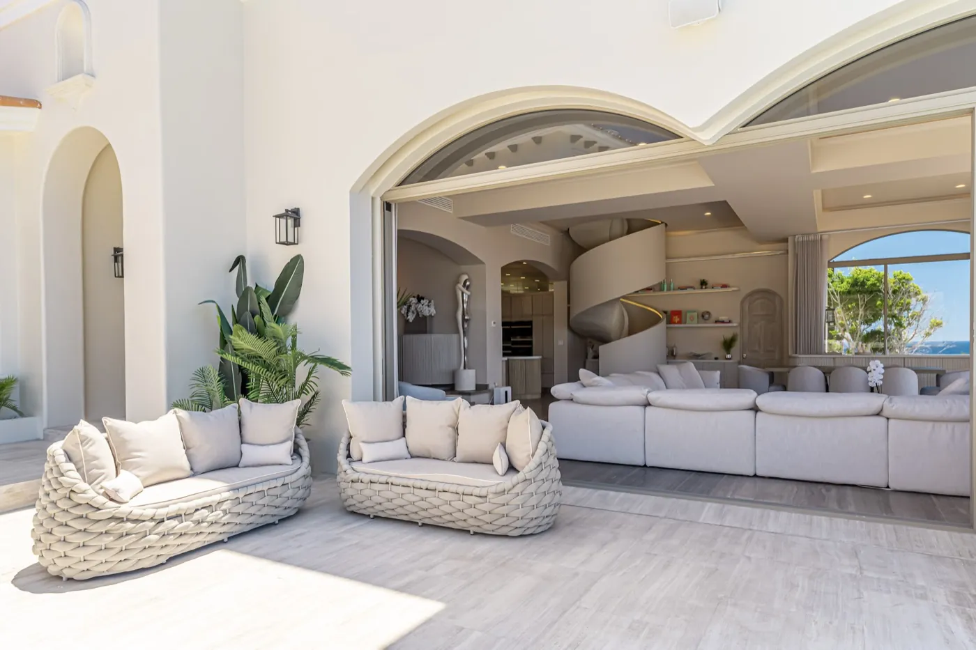 Covered terrace with woven daybeds opening to a living room and sculptural spiral staircase.