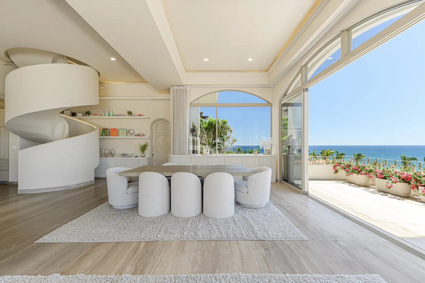 Dining room beside a sculptural staircase, sliding glass opening to a bougainvillea terrace and ocean.