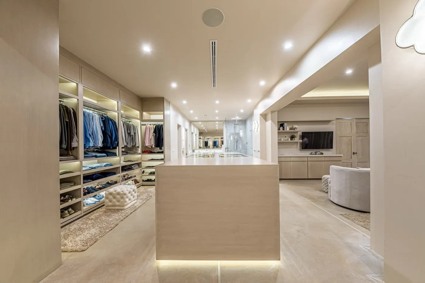 Expansive dressing room with backlit open wardrobes and a central oak island under soft light.