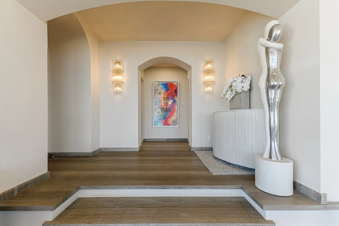 Arched entrance hall with timber floors, a polished figurative sculpture and warm wall sconces.