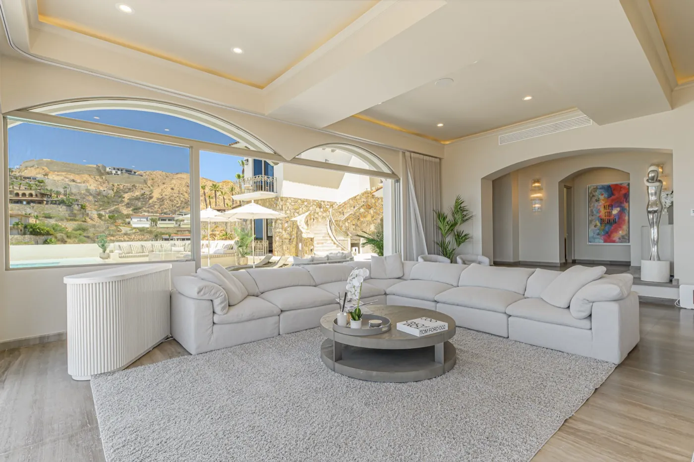 Spacious great room with cream sofas, a round coffee table and arched windows onto the hillside.