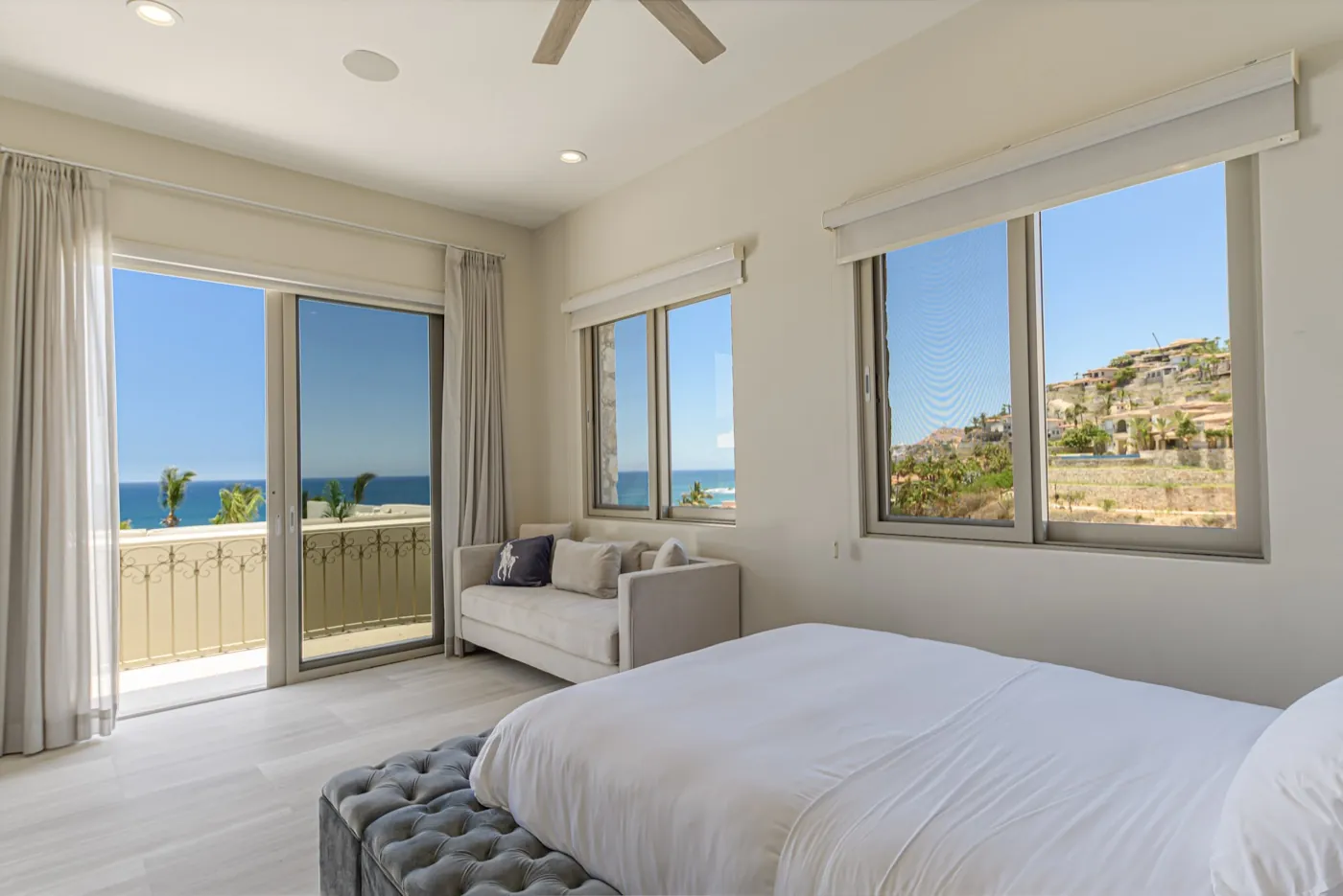 Calm guest bedroom with crisp white bedding, a velvet bench and sliding doors framing a blue sea view.
