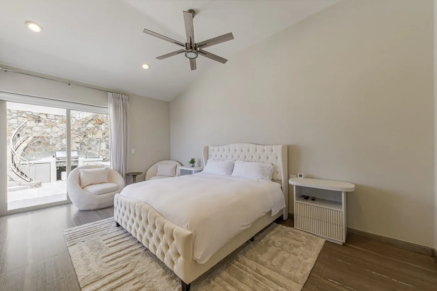 Guest bedroom with a tufted cream bed and sliding doors onto a private stone courtyard.