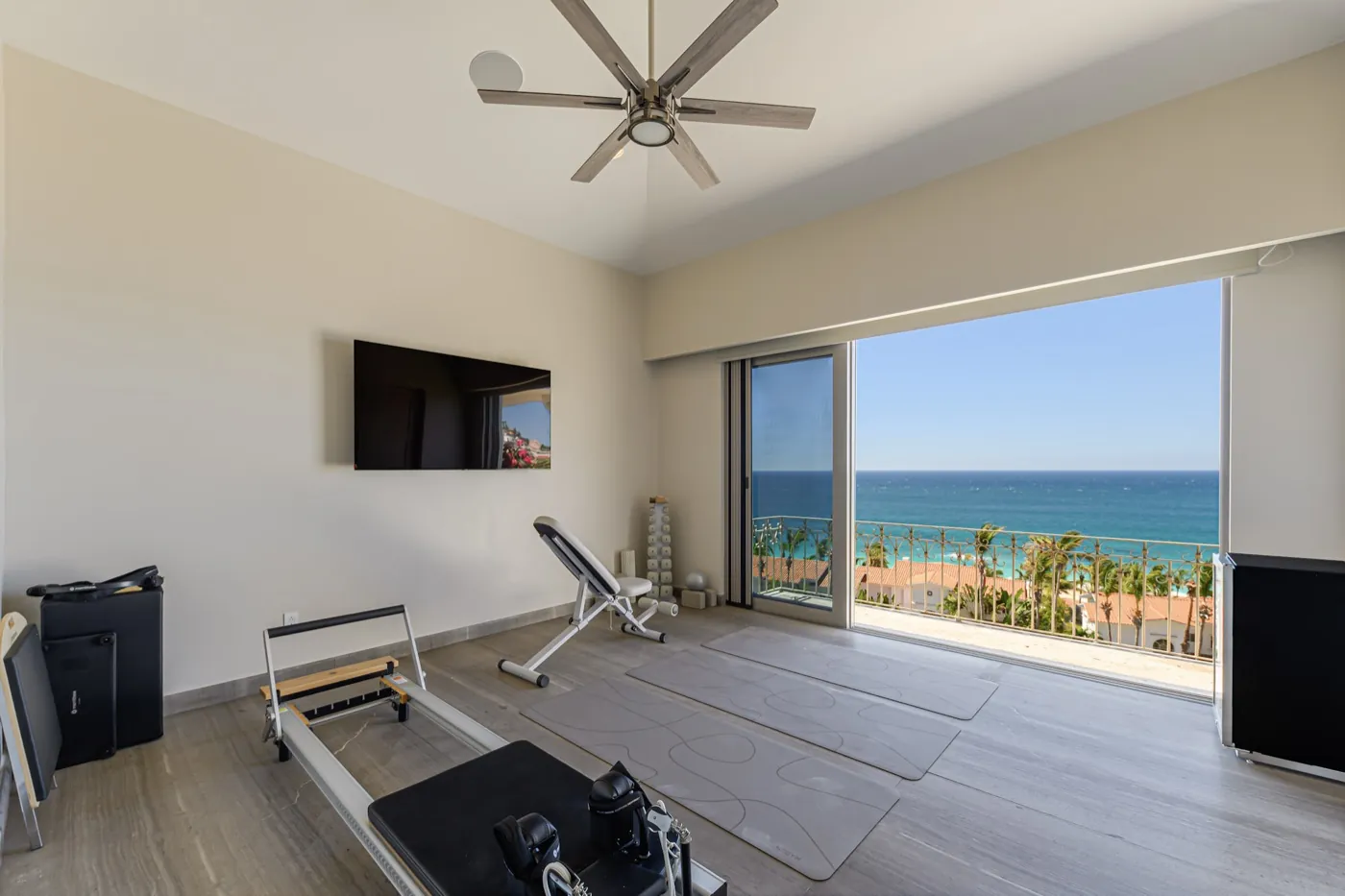 Home gym with a Pilates reformer and weights bench beside sliding doors open to the sea.
