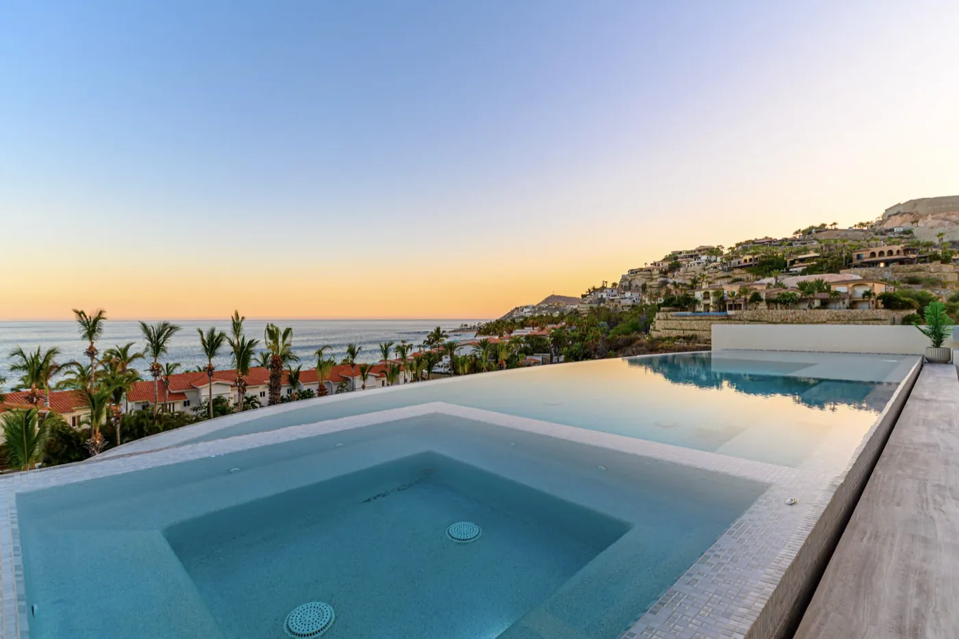 Infinity pool and sunken spa overlooking the coastline beneath a soft golden dusk sky.