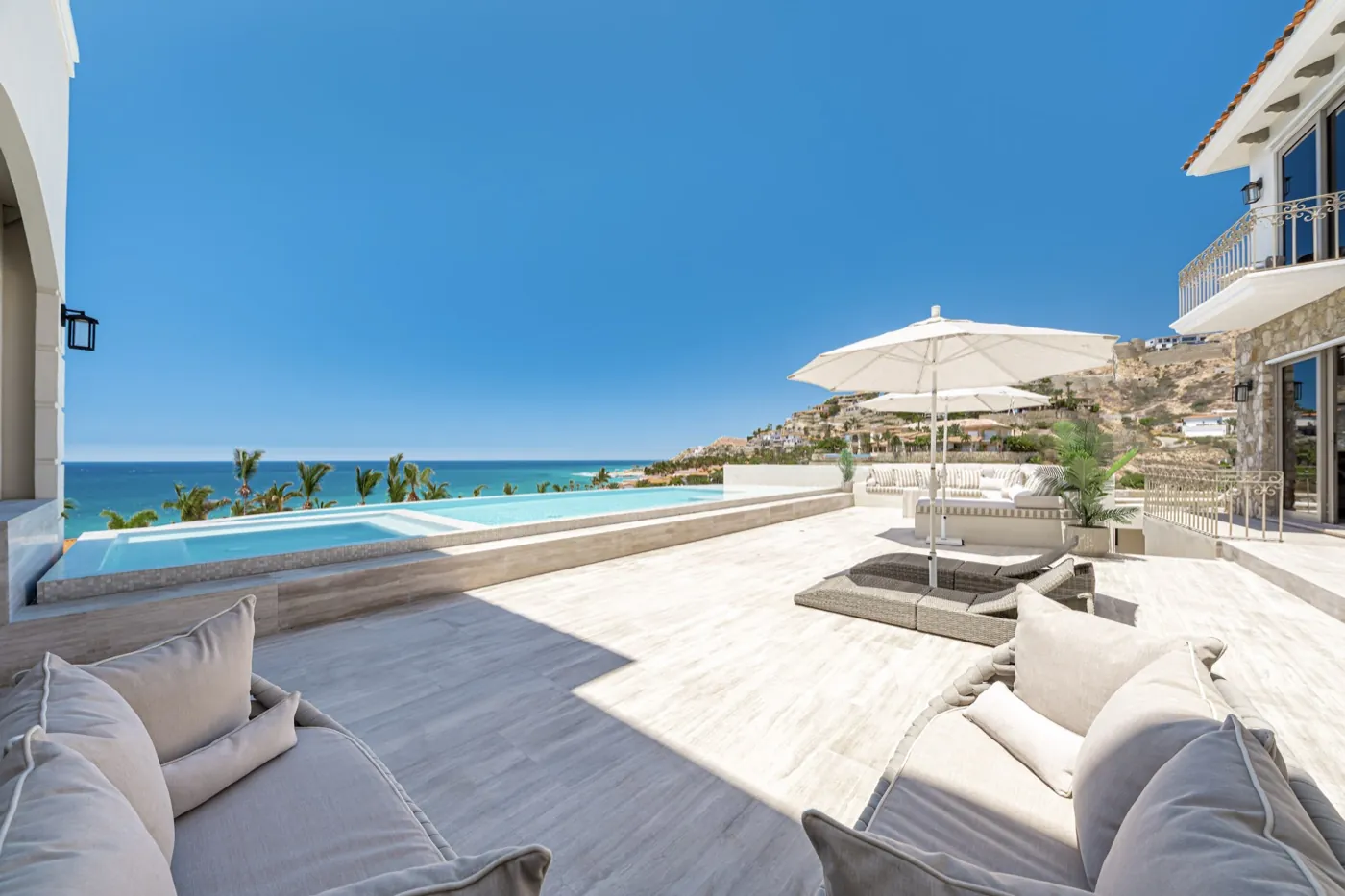 Travertine pool terrace with cushioned loungers, a parasol and an infinity pool above the ocean.