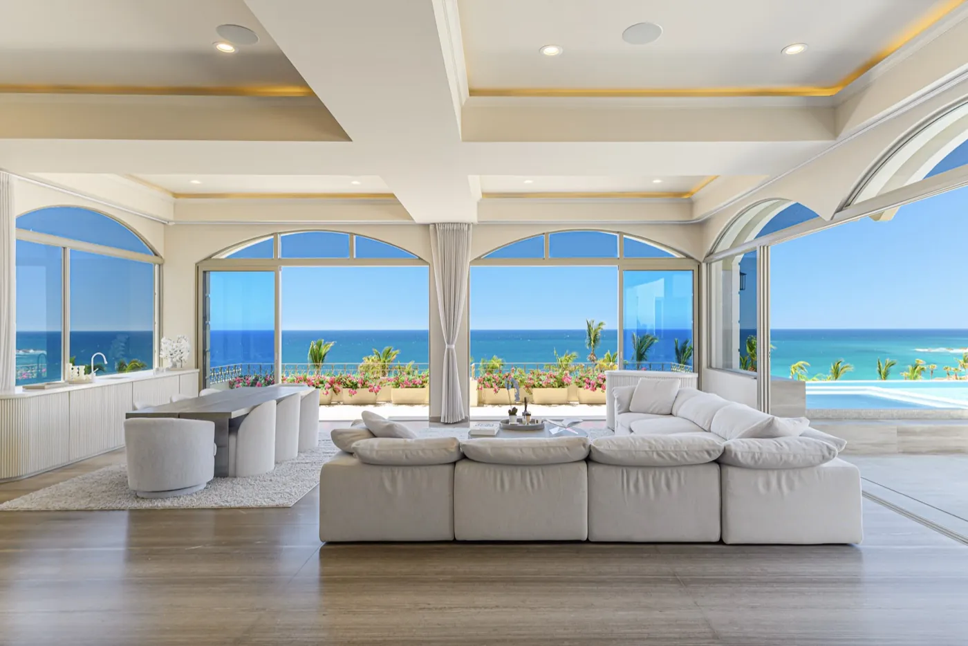 Open-plan living room with a pale sectional sofa, coffered ceiling and arched windows framing the sea.