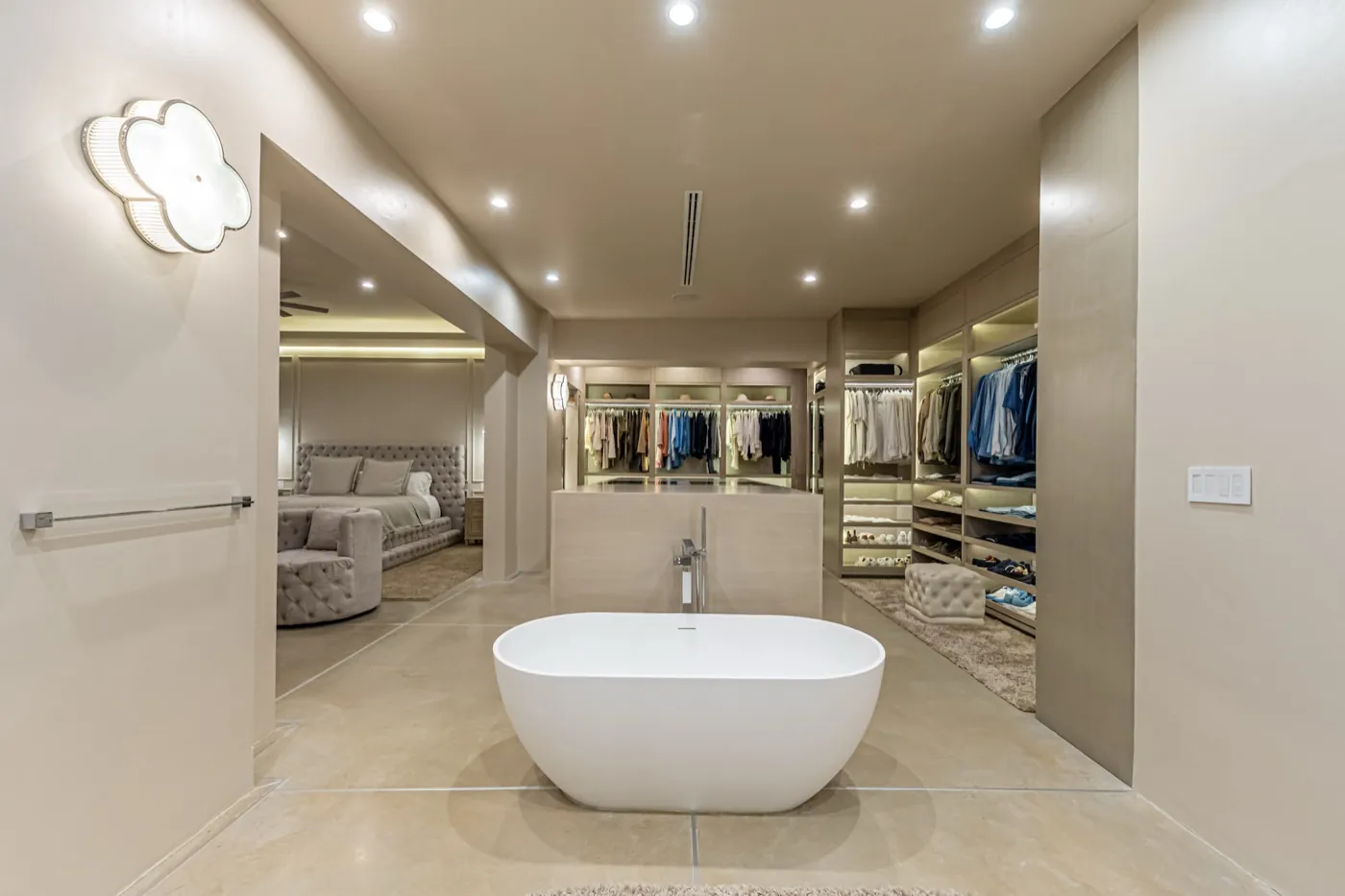 Master suite with a freestanding stone bath set before an open dressing room in warm neutral tones.