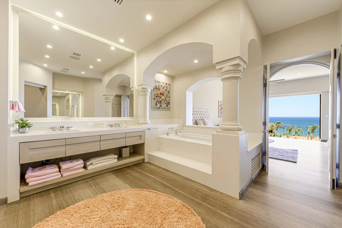 Master bathroom with twin vanity, soaking tub and stone columns, opening to a bedroom with sea views beyond.