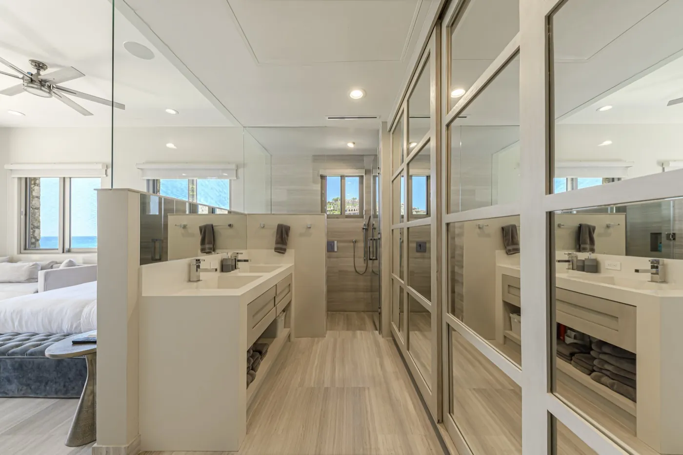 Master bathroom with twin stone vanity and walk-in shower beside a sea-view bedroom.