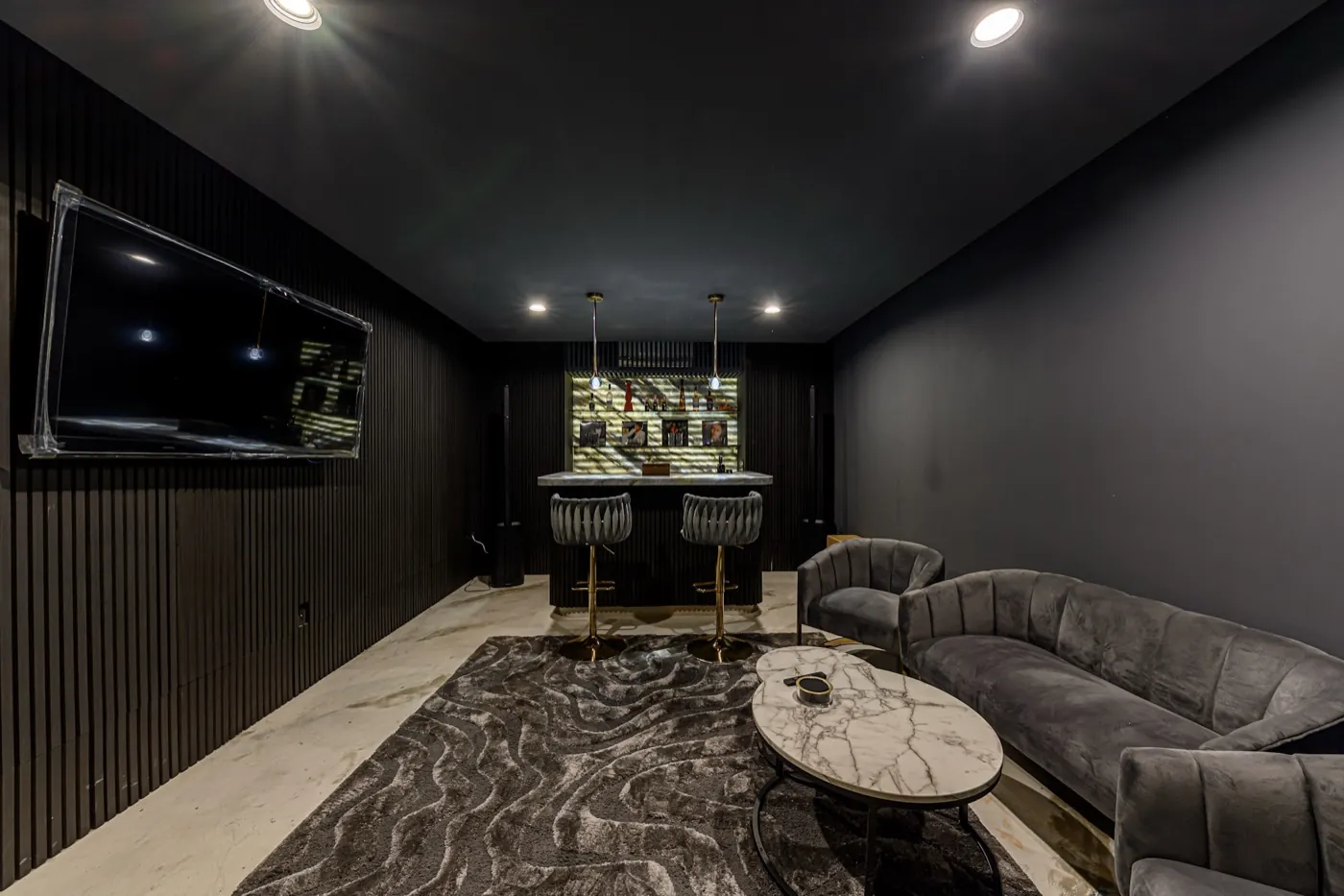 Darkly panelled media lounge with velvet seating, a backlit bar and a wall-mounted screen.