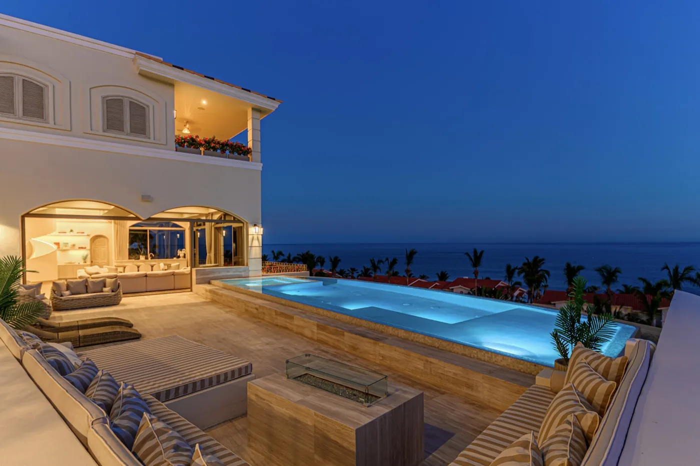 Terrace at dusk with a glass-sided fire pit, striped loungers and an infinity pool overlooking the sea.