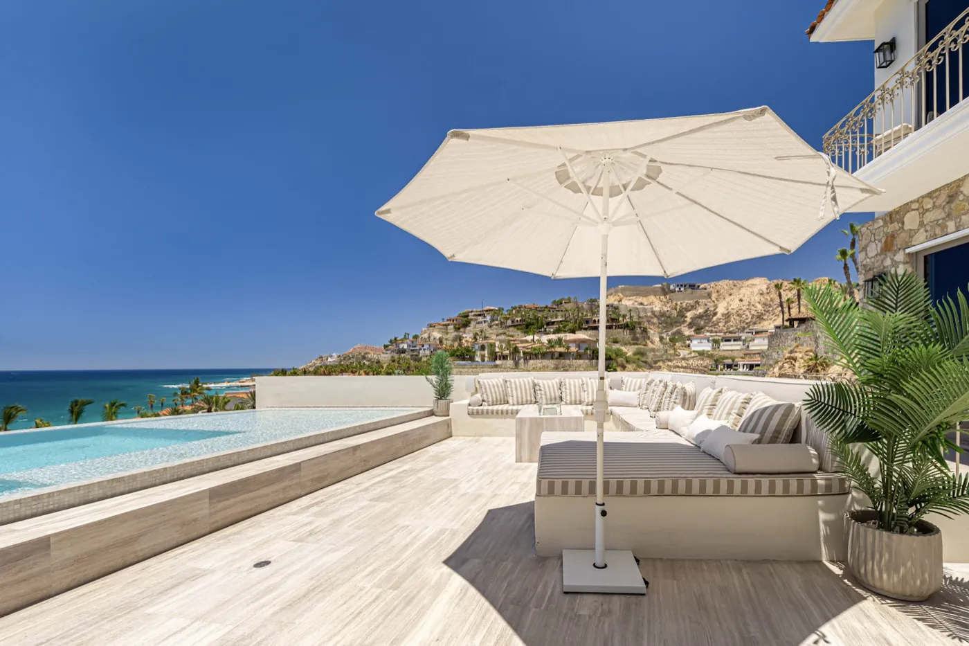 Sun terrace with striped daybed and parasol beside an infinity pool above the turquoise sea.
