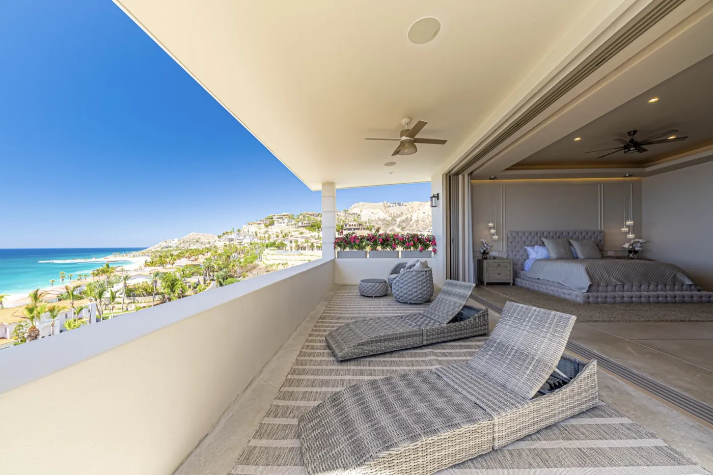 Primary suite balcony with woven loungers overlooking a turquoise bay and hillside coastline.
