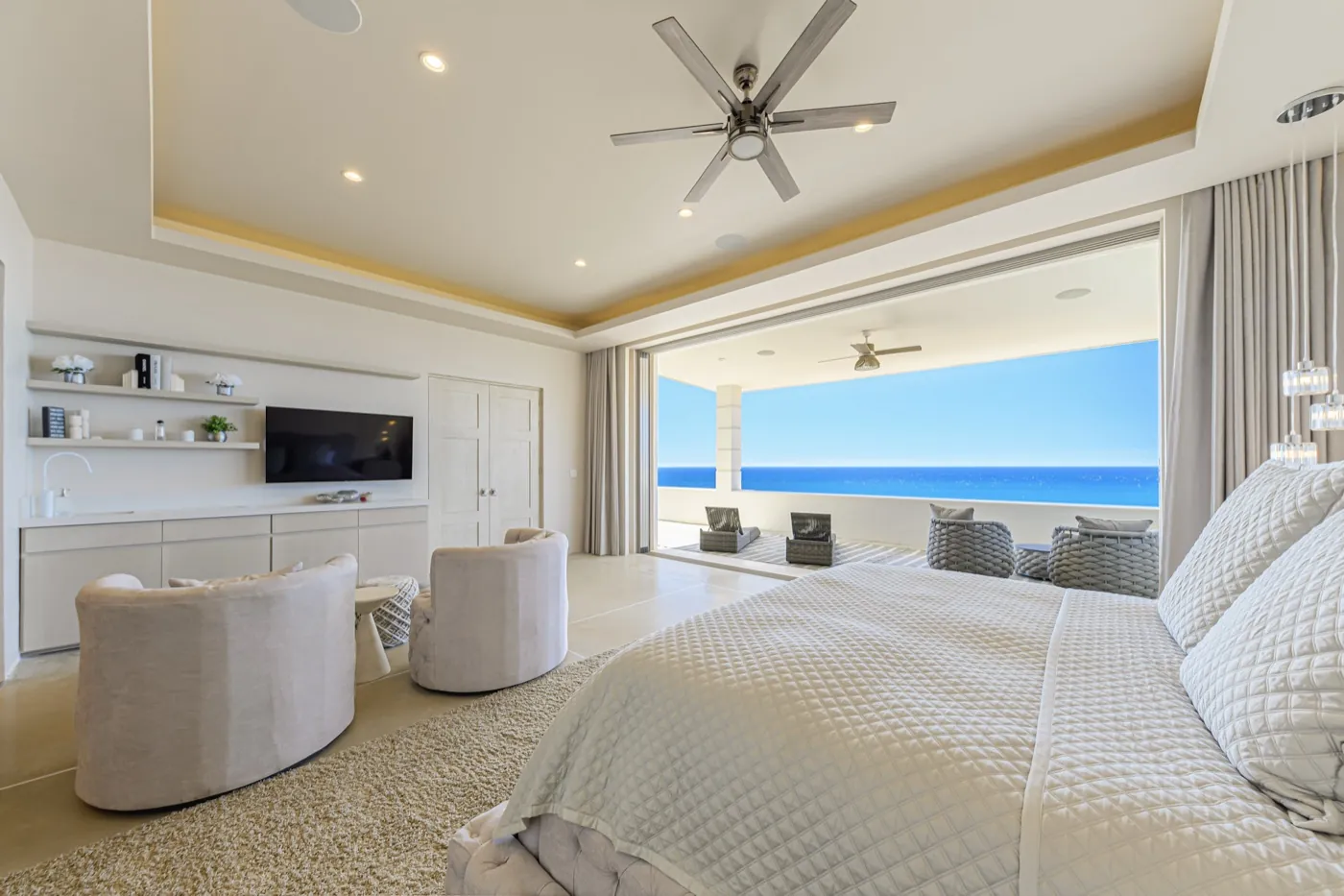 Primary bedroom in soft neutrals opening through sliding doors to an ocean-view terrace.