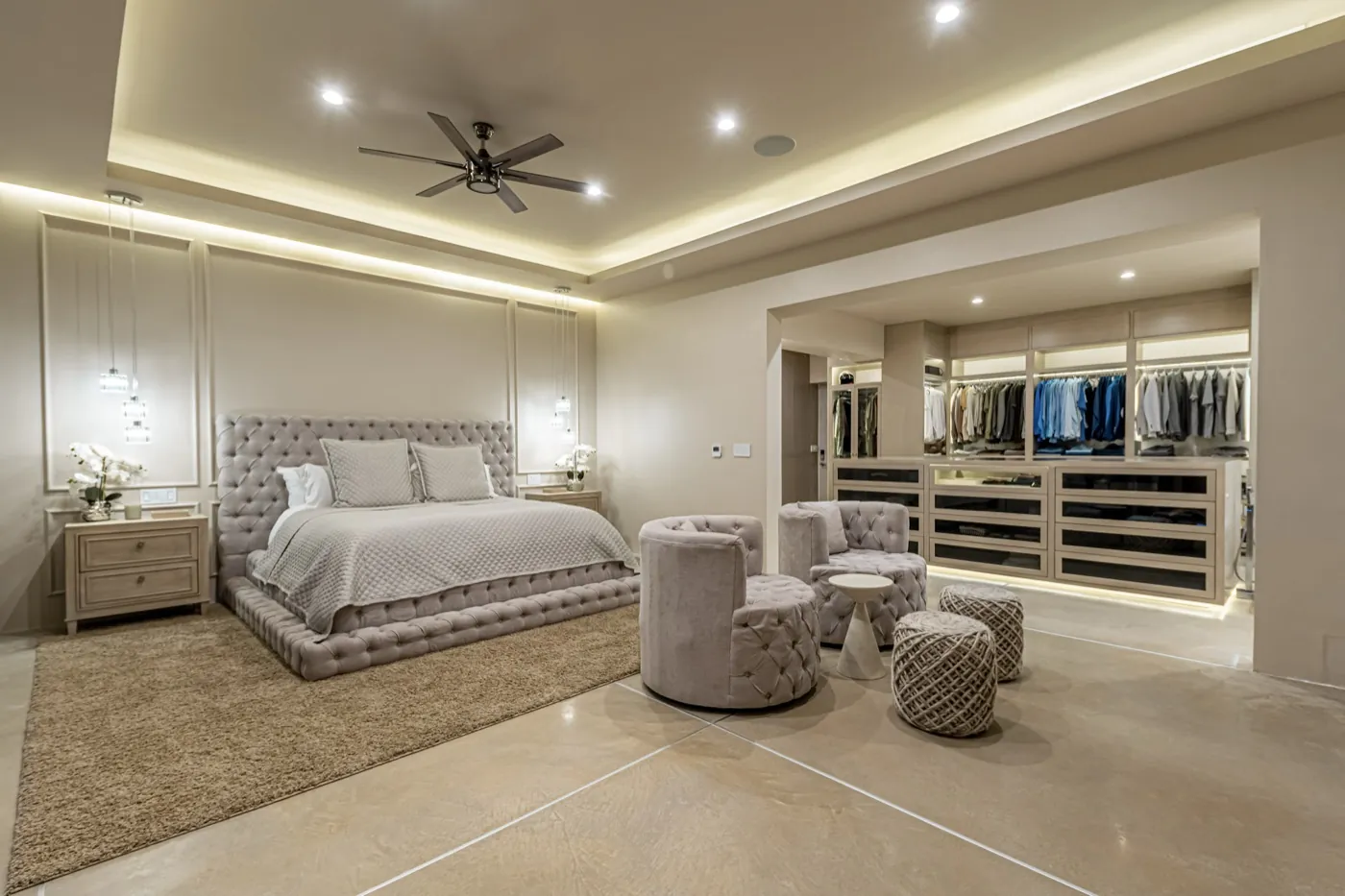 Primary suite with a tufted bed and softly lit walk-in dressing room beneath a coffered ceiling.