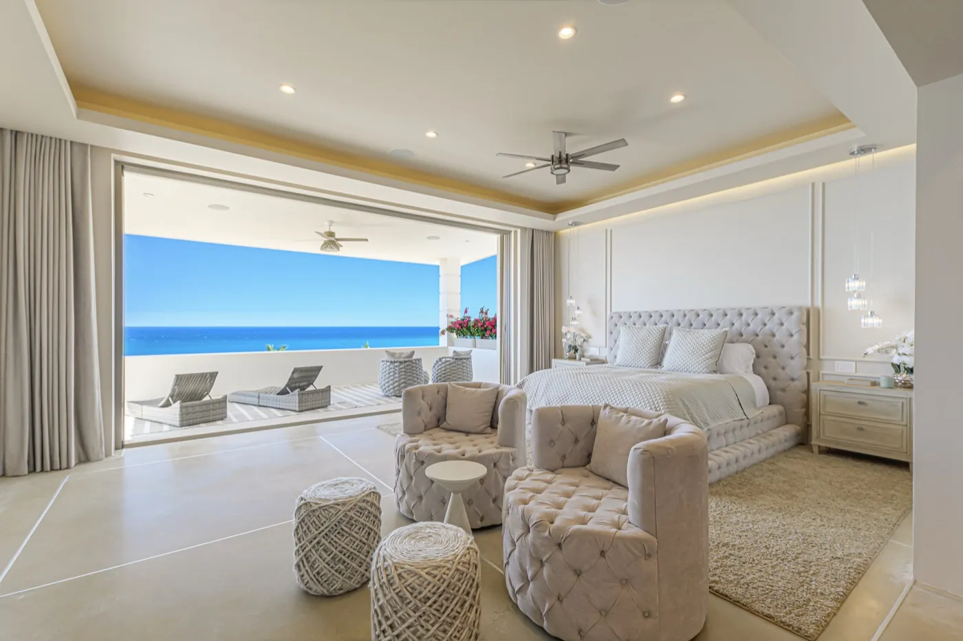 Primary suite with a tufted upholstered bed opening to a terrace and uninterrupted ocean horizon.
