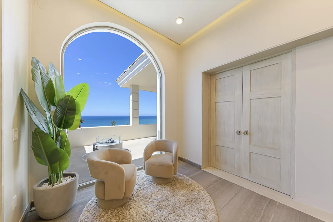 Sitting nook with boucle tub chairs framing an arched window onto the blue Sea of Cortez.