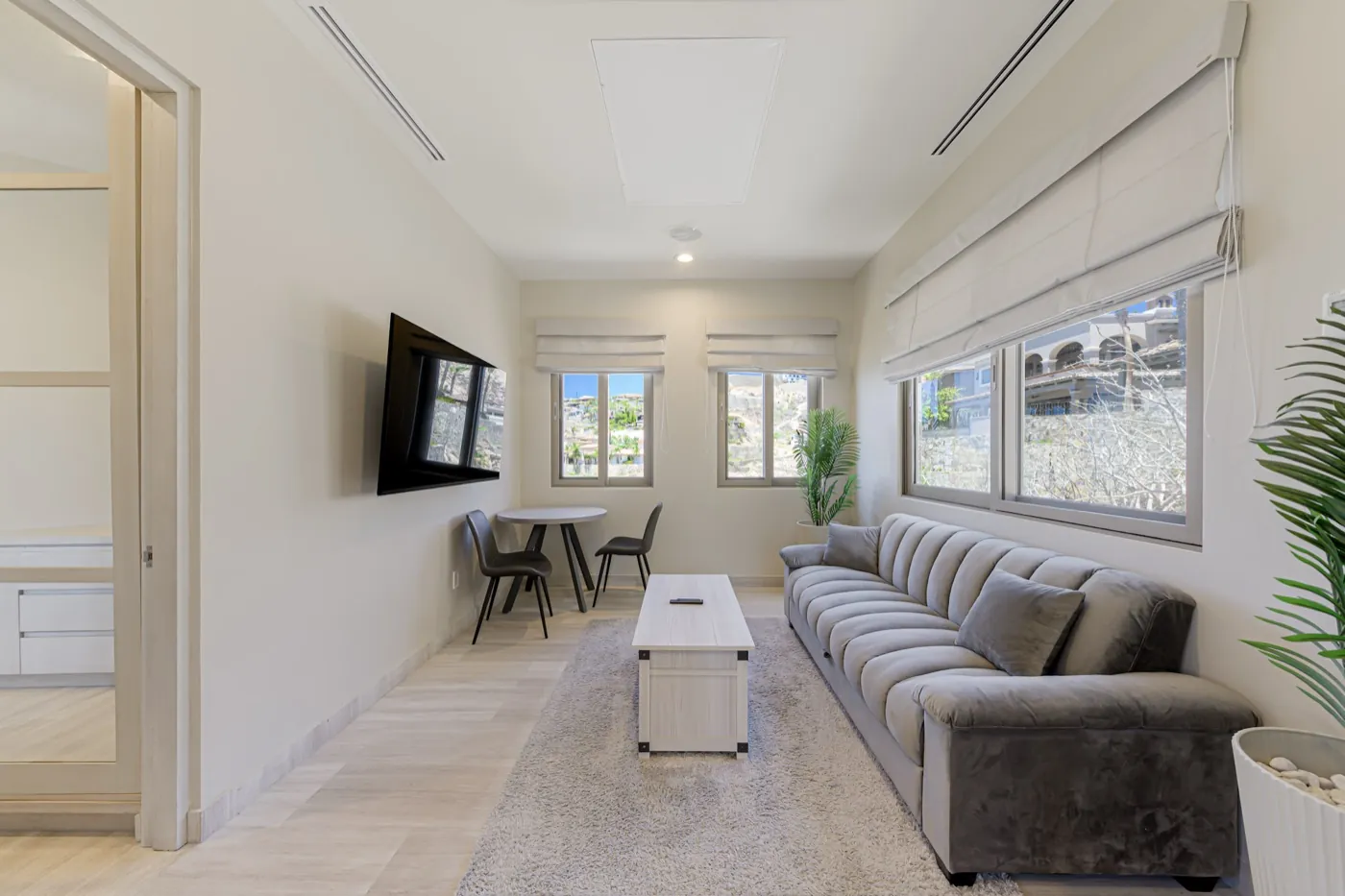 Calm sitting room with a grey sofa, breakfast table and windows framing the hillside.