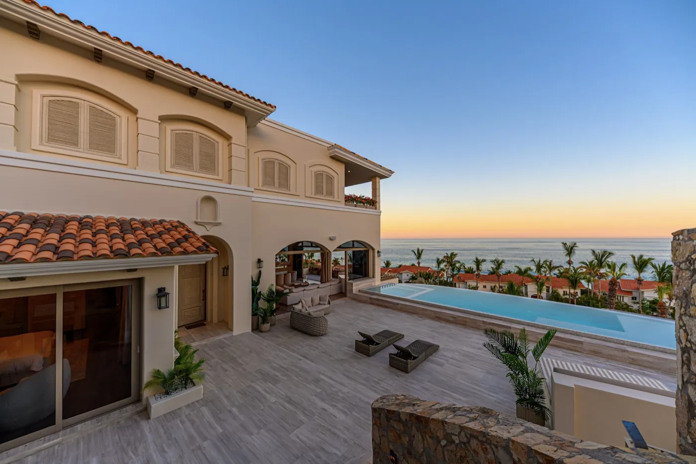 Upper terrace with loungers and an infinity pool framing the ocean under a tranquil sunset.