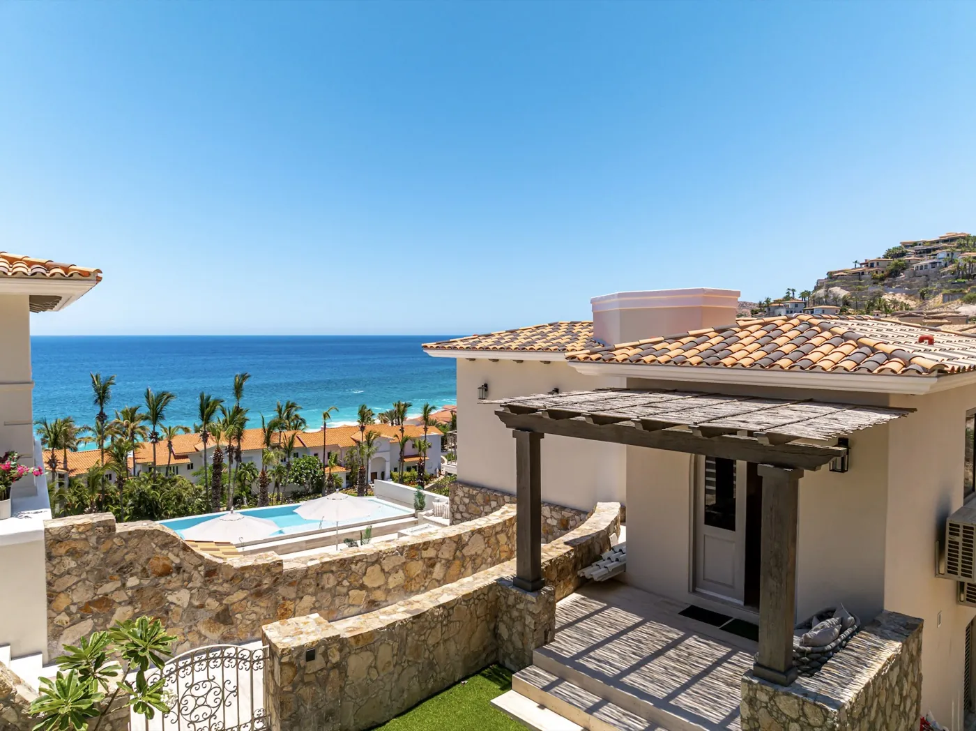 Tiled-roof terrace framing a sea view across rooftops, with a pool set into stone terracing below.