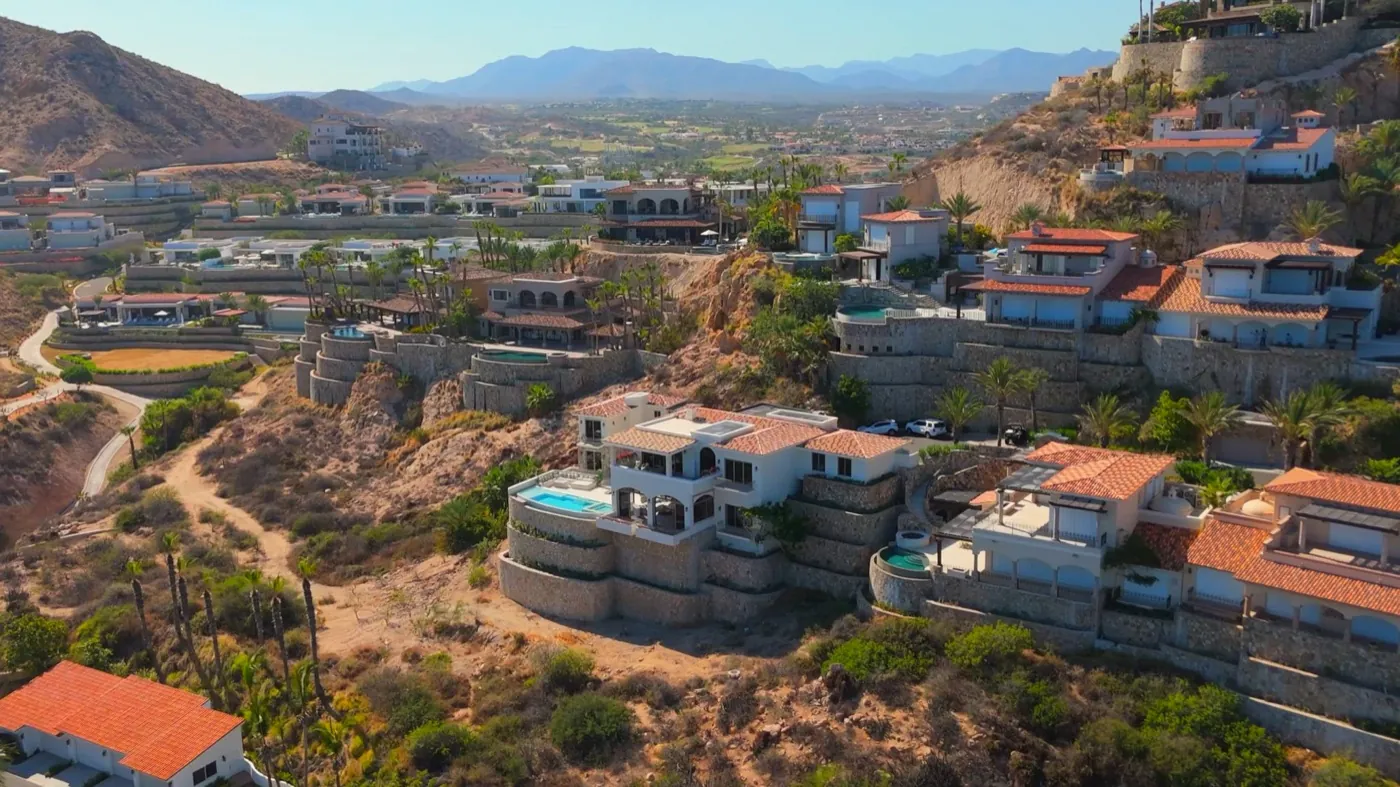 Aerial view of the hillside villa and its pool set among desert ridges and neighbouring estates above the coast.