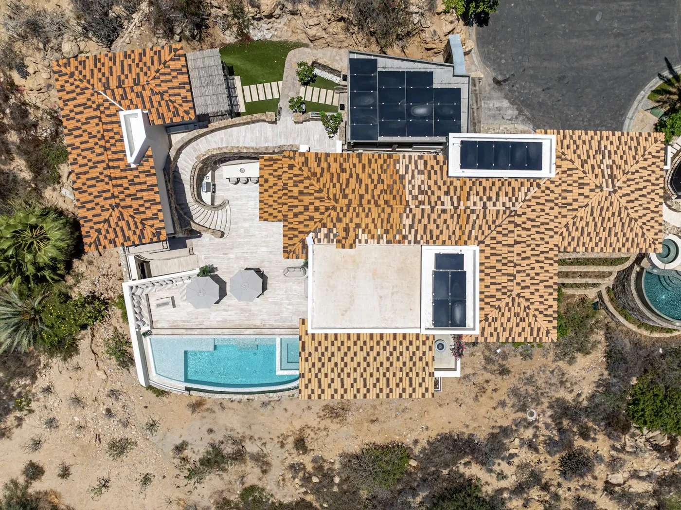 Aerial view of the villa's terracotta-tiled roofs, solar panels and turquoise pool set into desert scrub.
