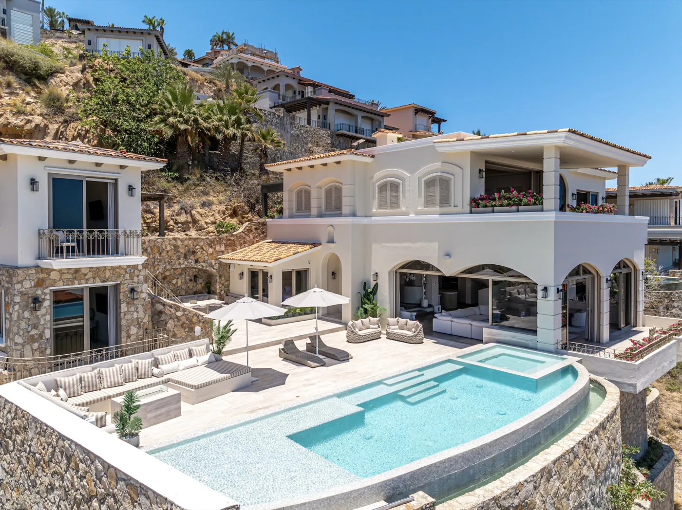 Hillside villa exterior with a curved pool, loungers and shaded terrace above the bay.