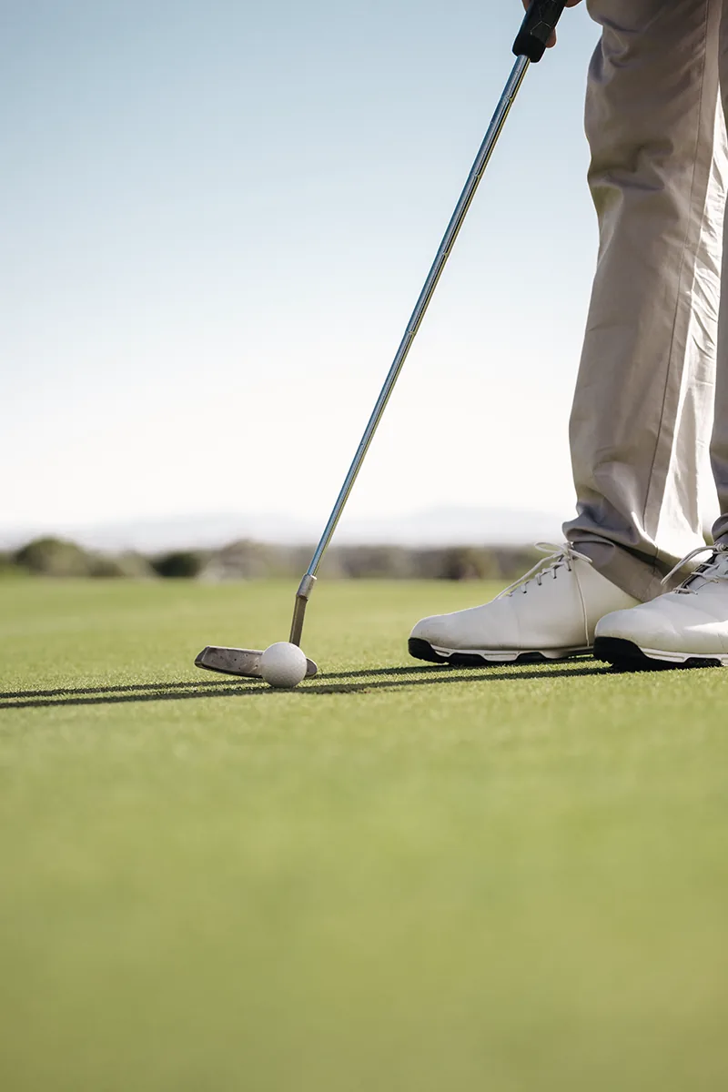A golfer at address over the ball on a sunlit Los Cabos fairway, the hills beyond.
